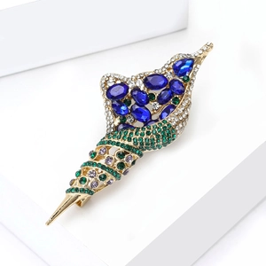Détail macro d'une broche conque de luxe avec gemmes bleues et cristaux verts sur blanc
