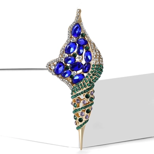 Broche élégante en forme de coquillage doré avec cristaux bleus et verts sur socle blanc
