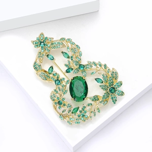 Macro detail of golden metal brooch featuring emerald green gemstones in floral pattern