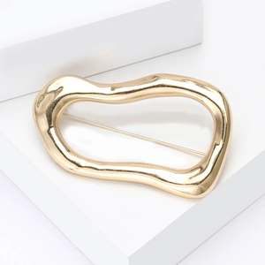 Detail of a golden irregular fluid-shaped alloy brooch with a glossy mirror finish