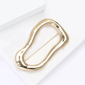 Detail of a wavy irregular gold brooch on a white geometric minimalist display stand