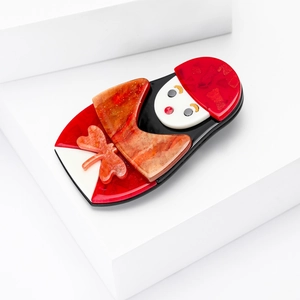 Détail d'une broche poupée russe en acrylique avec des finitions pailletées ambrées
