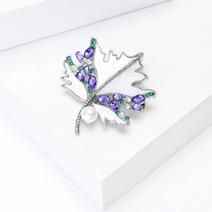 Macro shot of maple leaf brooch with natural shell, purple crystals and a white pearl
