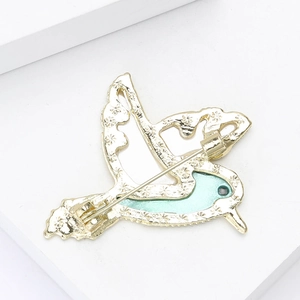 Vue arrière d'une broche colibri dorée avec émail vert sur une plateforme blanche