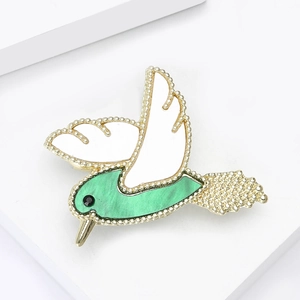 Broche colibri exquise avec monture dorée et nacre verte sur un fond blanc épuré
