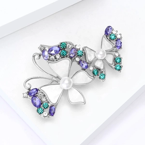 Detailed close-up of butterfly brooch with purple gems and white pearls on silver metal