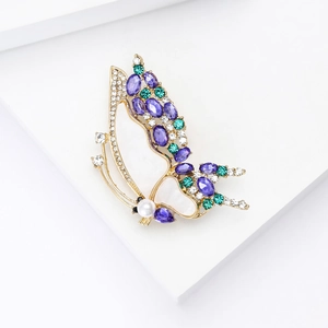 Détail de la broche papillon avec pierres mauves, strass verts et une perle blanche