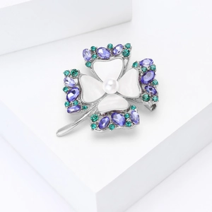 Detalle macro del broche de trébol en nácar con gemas púrpuras y una perla blanca