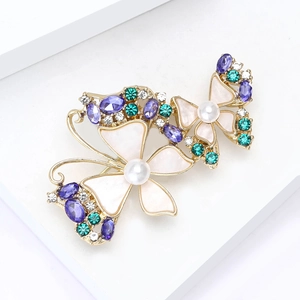 Elegant gold butterfly brooch with purple rhinestones and pearls on white platform
