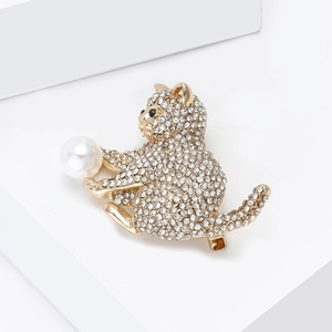 Vue détaillée d'une broche chat dorée sertie de strass avec une perle blanche élégante
