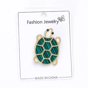 Detail of cute turtle brooch with green striped shell on white jewelry card