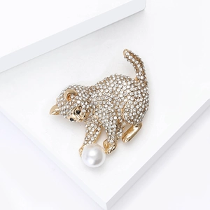 Détail d'une broche chat dorée avec des strass étincelants et une perle blanche