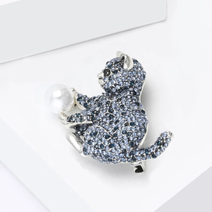 Détail d'une broche chat en strass bleus tenant une perle blanche sur un support blanc