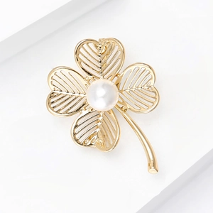 Macro view of gold four-leaf clover brooch featuring openwork design and white pearl inlay