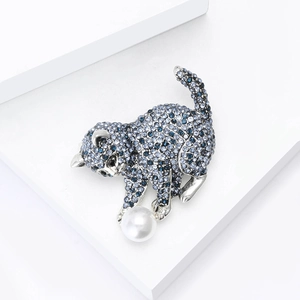 Broche chat raffinée avec strass bleus et une grande perle blanche sur un support chic