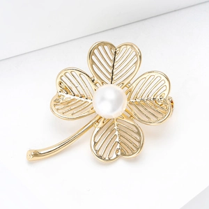 Close-up of golden hollow clover brooch with a pearl center and textured metal details