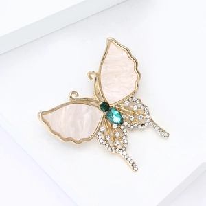 Elegant gold butterfly brooch with shell inlay and green gemstones on white background