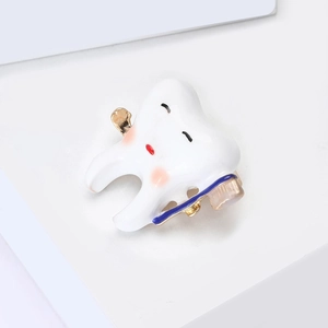Detail of cartoon tooth brooch with blue toothbrush and gold tooth accent on alloy metal