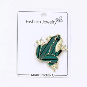 Detailed view of a green striped frog brooch pin with gold-tone edges on display card