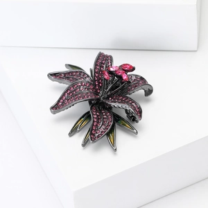 Close-up of lily brooch with pink crystals and green enamel leaf on a white block
