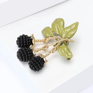 Detailed close-up of a golden enamel blackberry brooch with green leaves on white steps