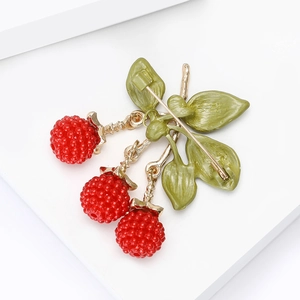 Detailed close-up of a red blackberry brooch with green leaves and a golden safety pin