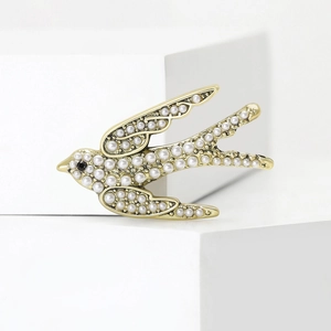 Élégante broche hirondelle dorée avec perles blanches et pierre noire sur présentoir