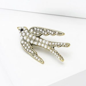 Détail d'une broche hirondelle vintage dorée avec perles incrustées et œil en gemme noire