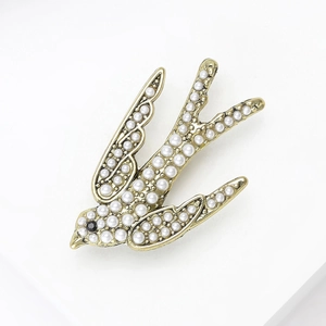 Vue détaillée d'une broche hirondelle dorée ornée de perles blanches et d'un cristal noir