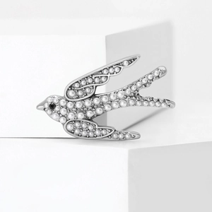 Broche hirondelle argentée avec perles blanches et gemme noire sur un support géométrique