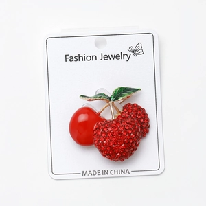 Detail of cherry brooch with red rhinestones and green enamel leaf on a white display card