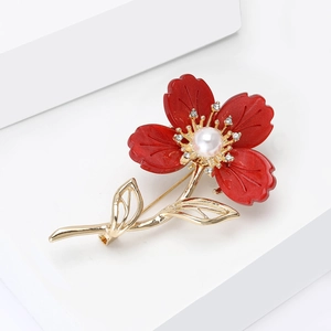 Gros plan détaillé d'une broche fleur en résine rouge avec perle et tige dorée