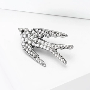 Détail macro de broche hirondelle argentée avec perles blanches et détail d'oeil noir