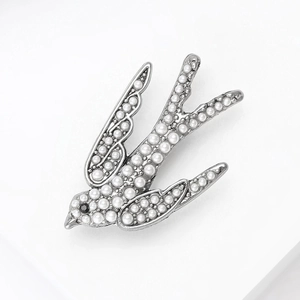 Détail de la broche hirondelle argentée ornée de perles blanches et d'un œil en gemme noire