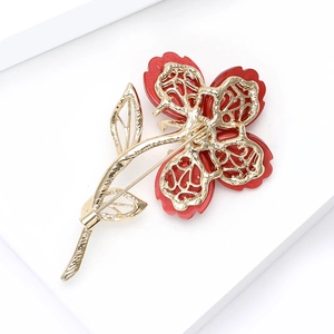 Vue détaillée d'une broche florale avec pétales en résine rouge et tige à feuilles dorées
