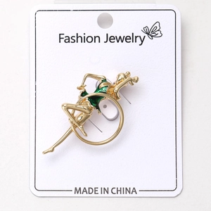 Détail d'une broche gymnaste en métal doré et émail vert sur carte à bijoux