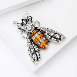 Vintage alloy bee brooch with orange enamel and sparkling crystals on a white stand