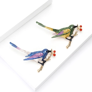 Elegante vogelspeldset met kleurrijke emaille vleugels op gouden tak met rode bessen