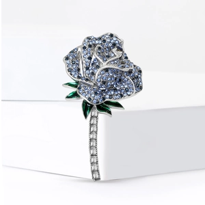Exquisite blue rose brooch with sparkling crystals and green leaves on white stand