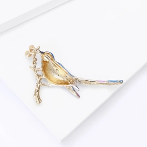 Detail van elegante gouden eksterbroche met blauw en paars emaille op een takje goud