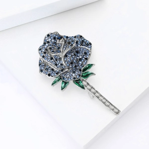 Close-up of blue crystal rose brooch with green enamel leaves on a white background