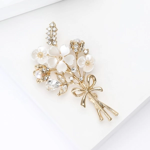 Détails d'une broche bouquet dorée avec des strass brillants et pétales blancs