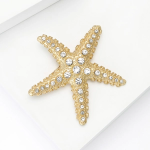 Broche étoile de mer en or mat avec strass brillants sur présentoir blanc minimaliste