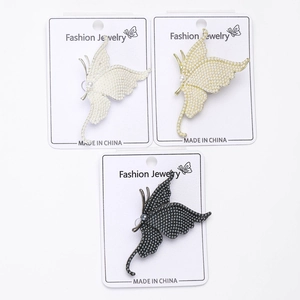 Detailed close-up of three pearl butterfly brooches in gold, silver and black finishes