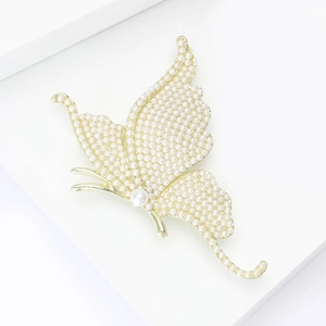 Detailed close-up of a gold butterfly brooch with inlaid white pearls on white background