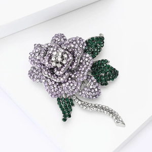 Elegant silver rose brooch with purple and green rhinestones on a white background