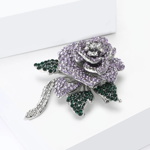 Macro shot of purple crystal rose brooch with green leaves on silver metal base
