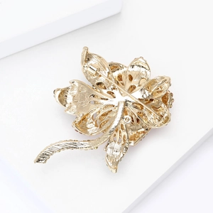 Detail of elegant gold flower brooch with hollow petals, rhinestones and safety pin