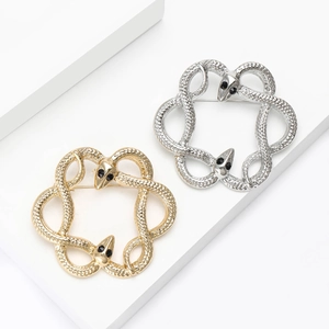 Polished gold and silver snake ring brooches with black gemstone eyes on white surface