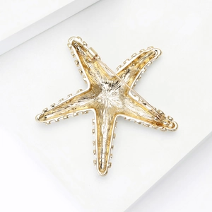 Vue arrière d'une broche étoile de mer dorée avec épingle de sûreté sur socle blanc